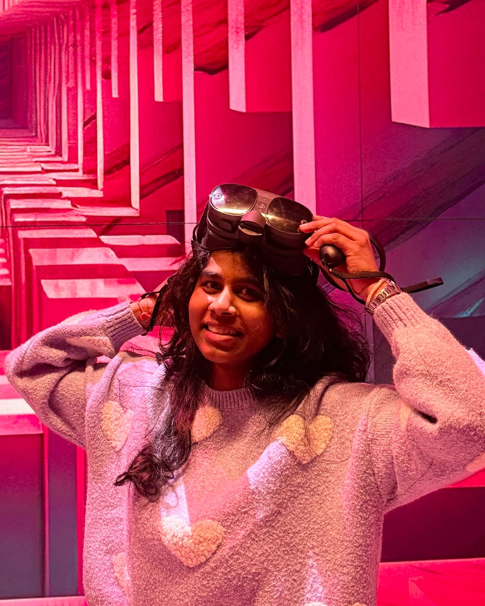 Jayasri Guthula lifting a VR headset, smiling in front of an immersive pink installation